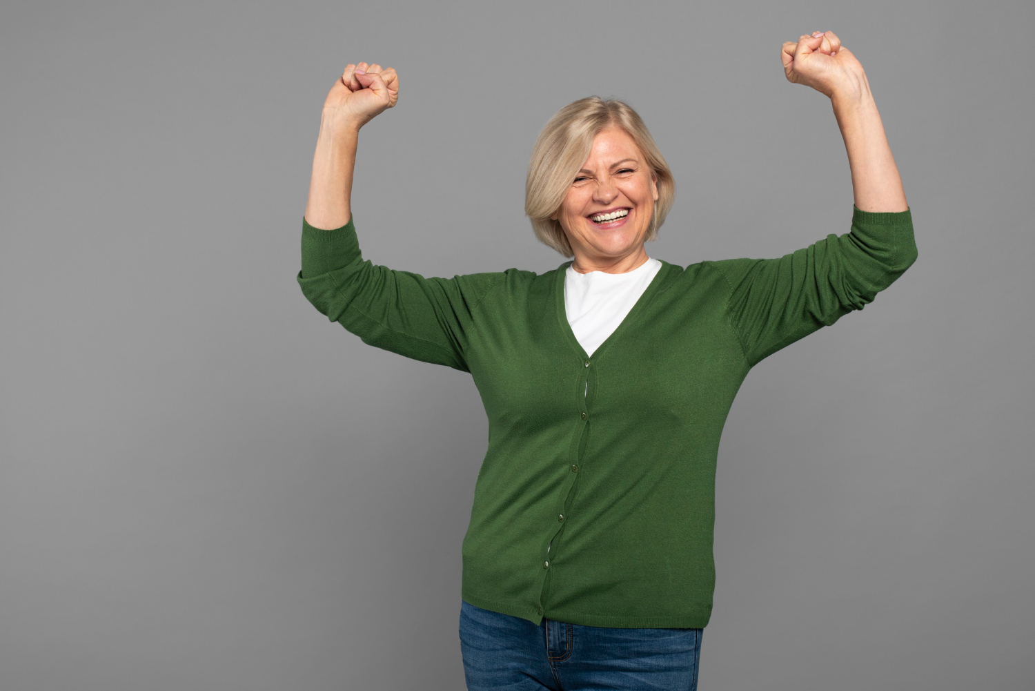 A smiling woman in green holds her fists above her head.