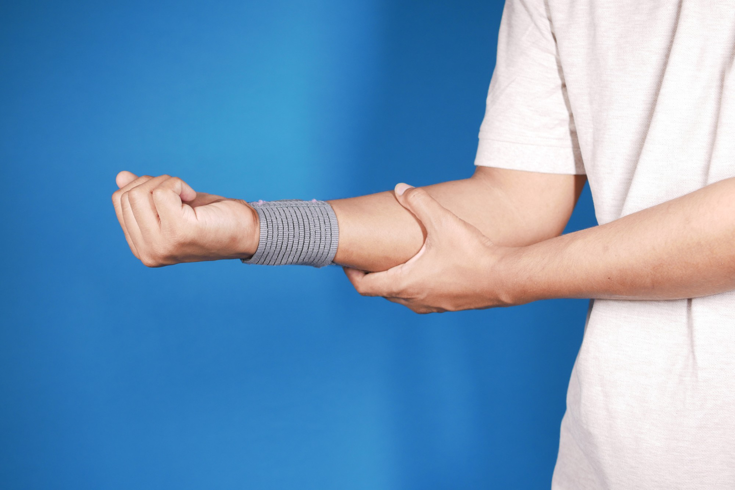 A man's right arm is held out in front of the man. There is a wrap on the wrist. The man is holding his right forearm with his left hand.