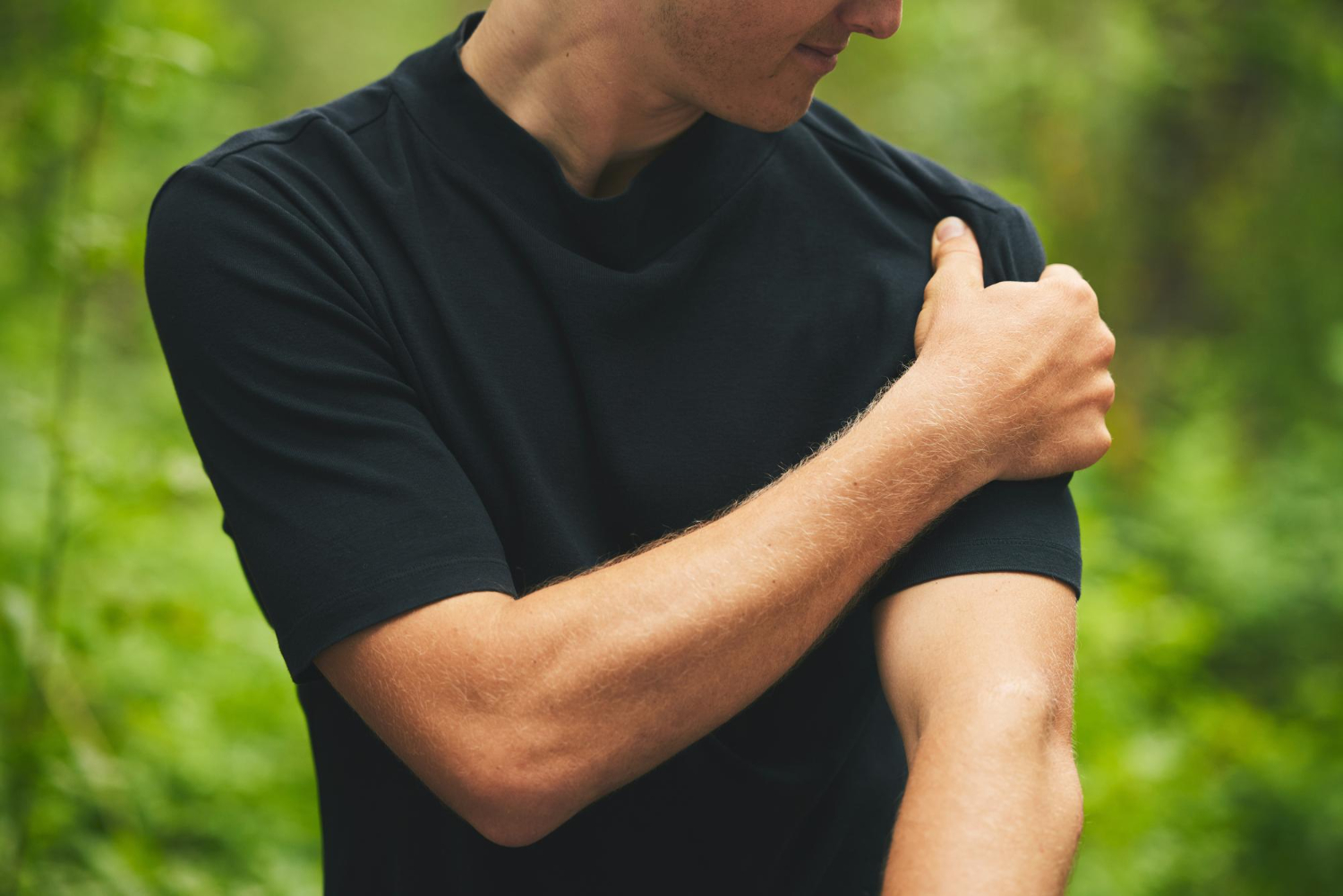 A man in a black shirt holding his left shoulder with his right hand.