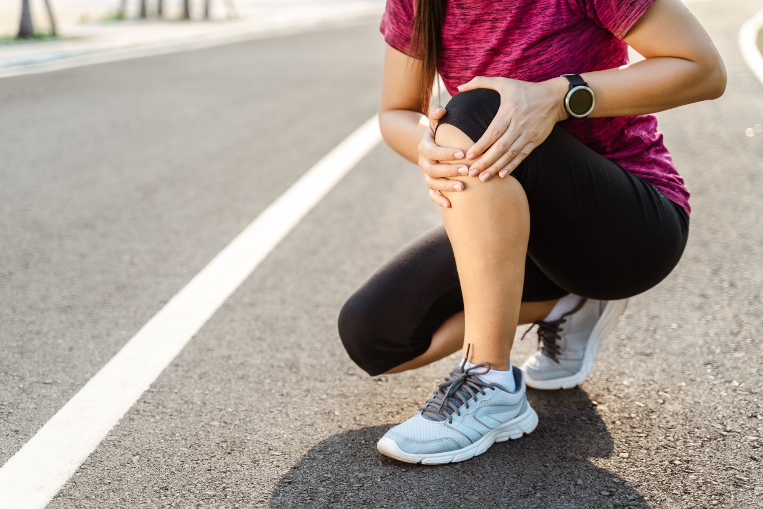 Female runner crouching on a running path, holding her sore knee.